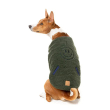 Load image into Gallery viewer, Dog sitting side-on wearing the dark moss sherpa FuzzYard reversible jacket, showing the embroidered smiley face on the back.