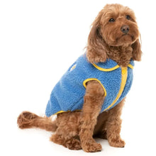 Load image into Gallery viewer, Dog sitting and wearing the FuzzYard Hana Dog Jacket in blue, showing the cosy sherpa texture and smiley flower patch.

