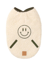 Load image into Gallery viewer, Beige sherpa dog jacket with embroidered green smiley face and quilted sage trims.
